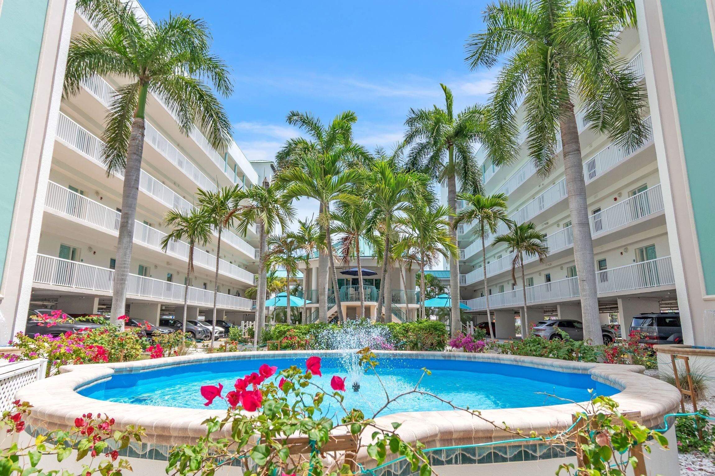 A hotel with a central pool, surrounded by palm trees and balconies.