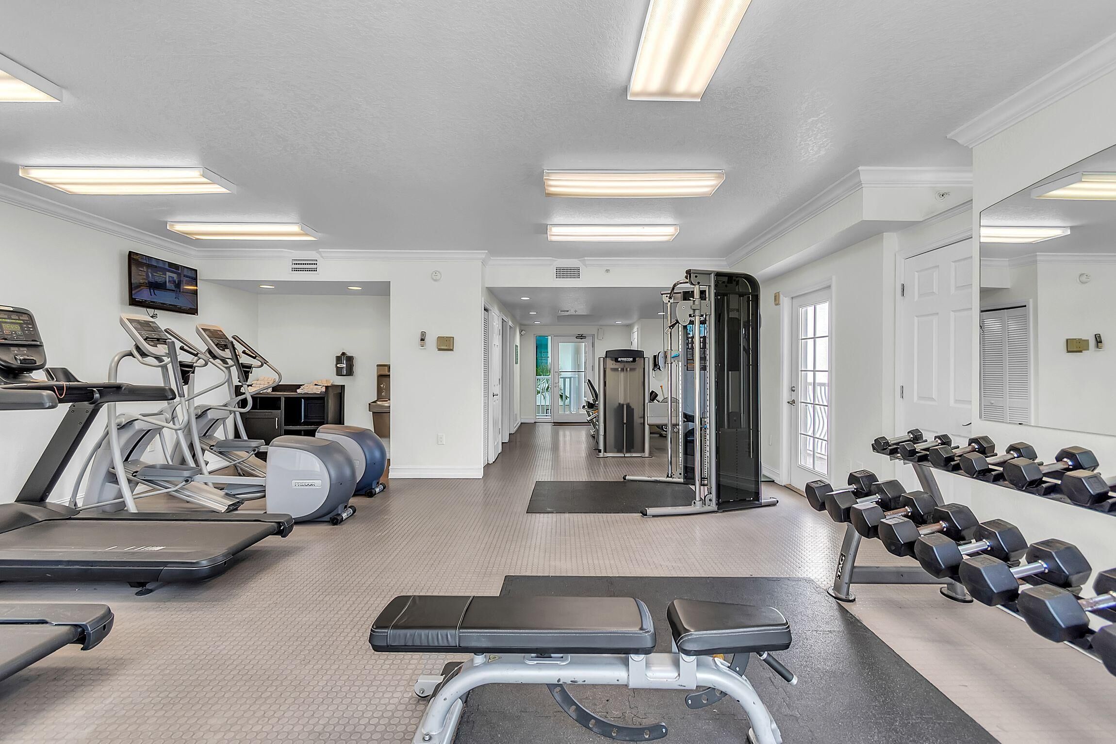 A gym with treadmills, elliptical machines, a bench press, and dumbbells.