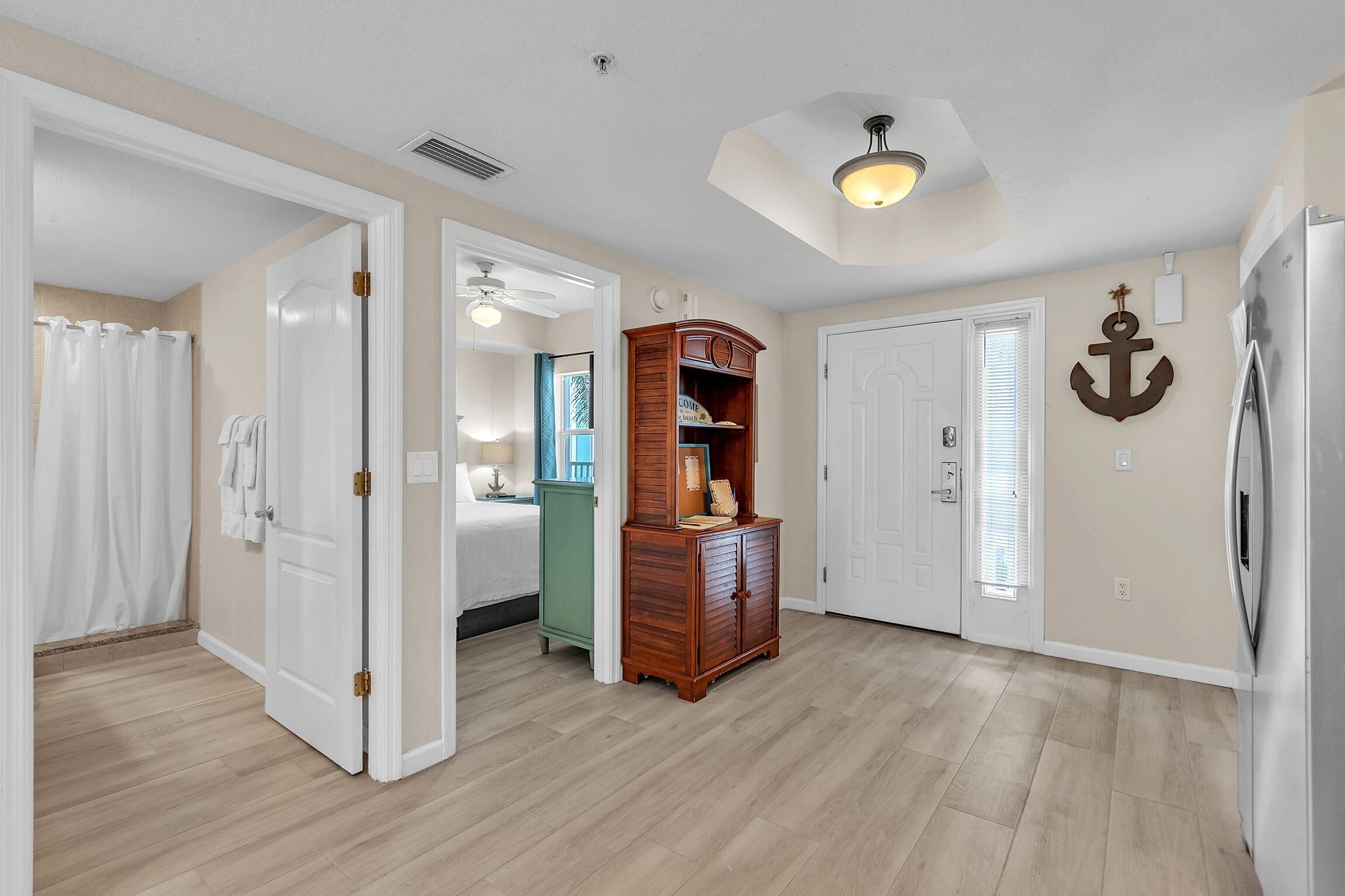 A spacious room with a wooden cabinet, a bed with white curtains, and a door leading to another room.