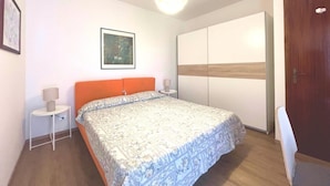 Ein Schlafzimmer mit Bett, Nachttisch, Wandbild, Kleiderschrank und einer Tür.