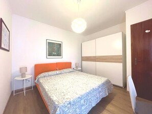 A bedroom with a bed, a nightstand, a wall-mounted artwork, a wardrobe, and a door. - Sunny Beachside Apartment in Grado (Grado)