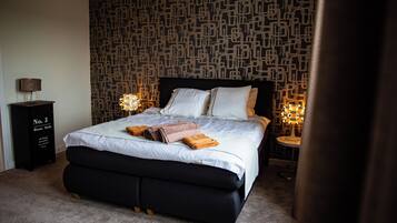 A neatly made bed with pillows and a blanket, a bedside table with a lamp, and a wall with a geometric pattern.