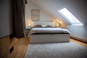 Una camera da letto con soffitto spiovente, un letto contenitore, due comodini e un lucernario.