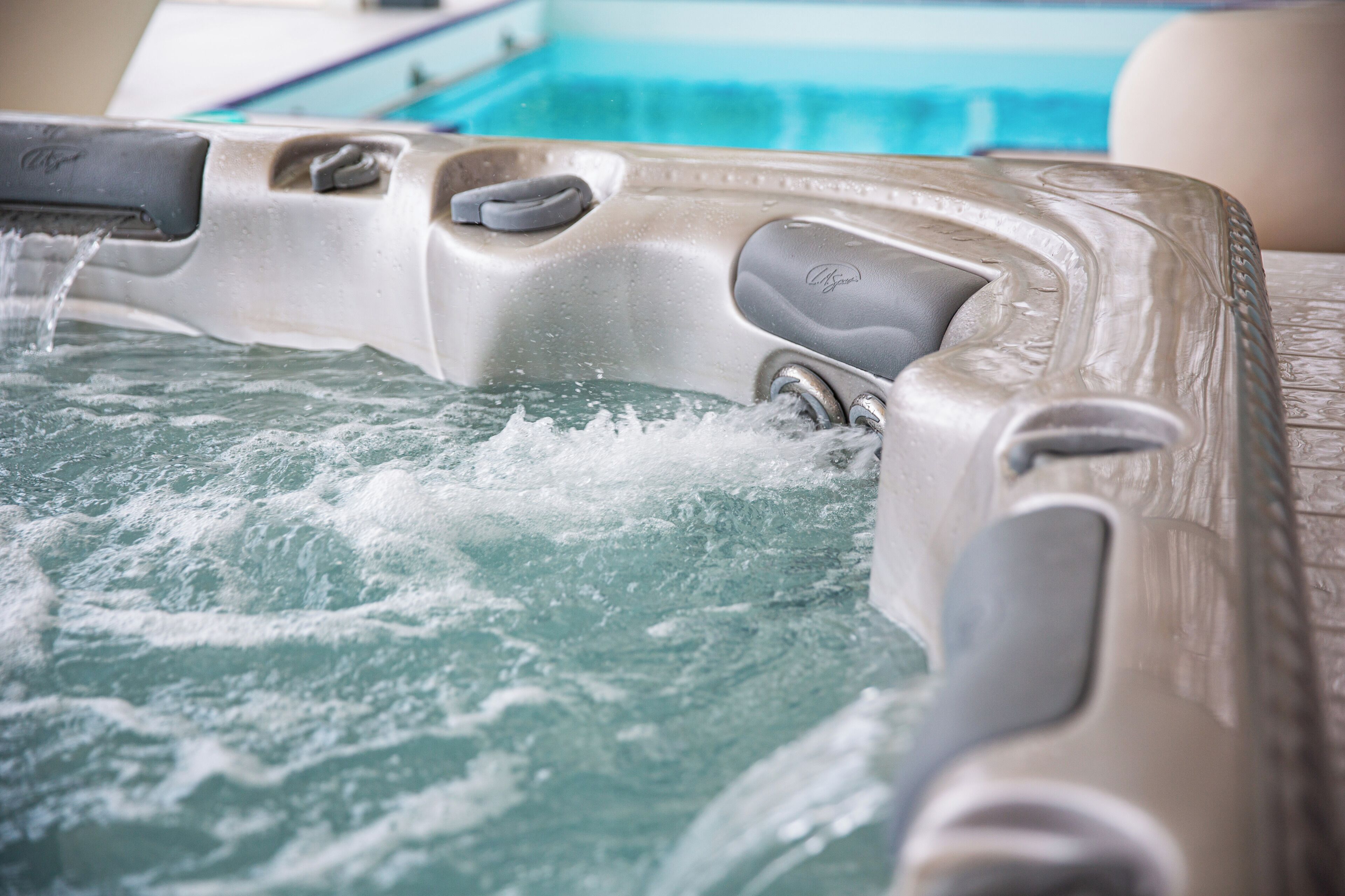 Een whirlpool met waterstralen, een bedieningspaneel en een zwembad op de achtergrond.