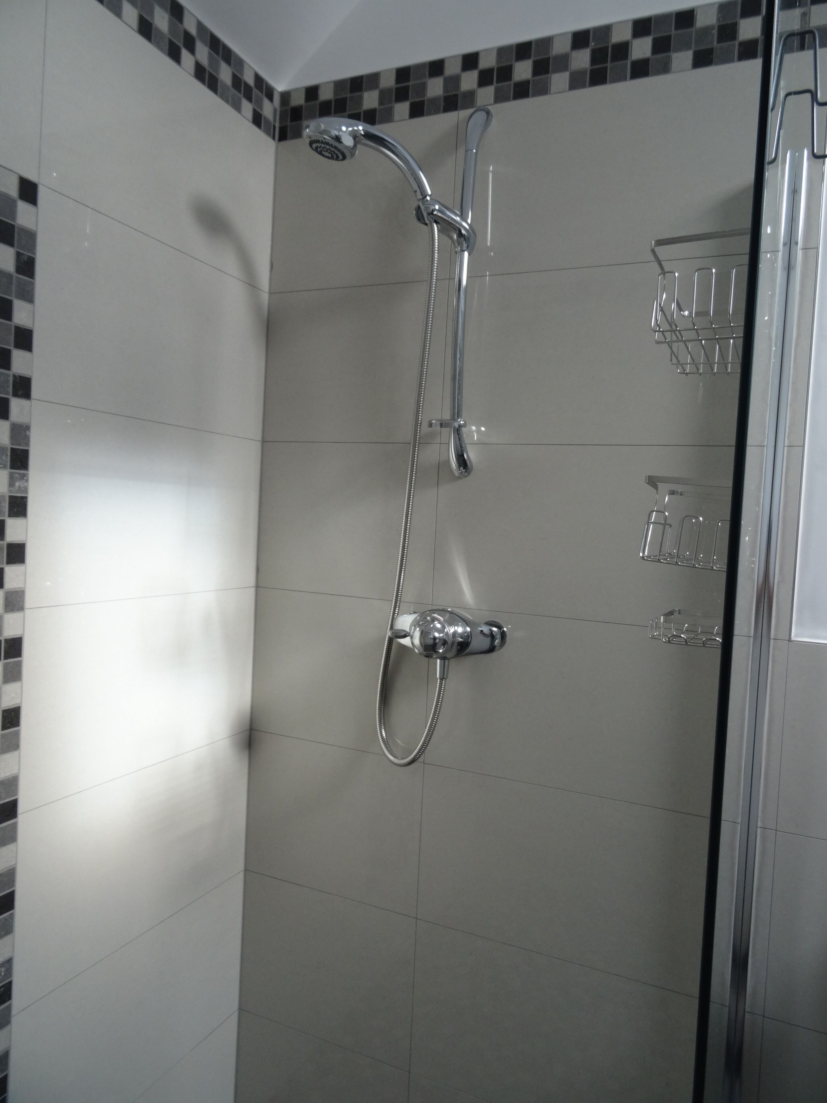 A shower with a handheld showerhead and a wall-mounted faucet.