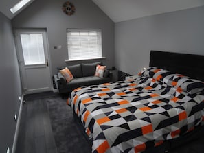 A bedroom with a bed, a sofa, a window, and a door.