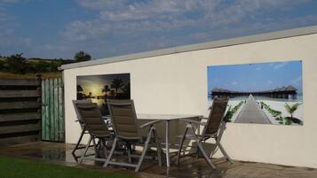Patio con tavolo e sedie, recinzione in legno e vista su un resort balneare attraverso una finestra.