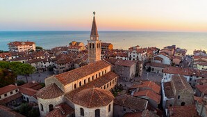 A historic town with a prominent church featuring a tall bell tower, surrounded by traditional buildings with red-tiled roofs. - Perfect Holiday Apartment for Five Guests in Grado (Grado)