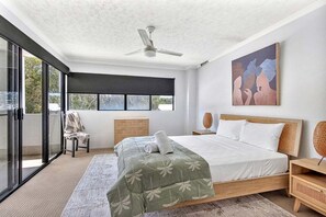 A bedroom with a large bed, a ceiling fan, a window with a view, and a painting on the wall. - The Beach Pad - Mudjimba (Sunshine Coast)