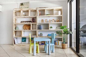 A room with a wooden bookshelf, two chairs, a small table, and a potted plant. - The Beach Pad - Mudjimba (Sunshine Coast)