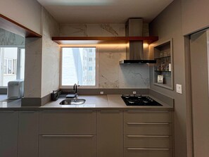 Une cuisine moderne dotée d’une cuisinière à gaz intégrée, d’un évier en acier inoxydable et d’une fenêtre donnant sur un immeuble.