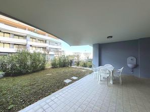 A courtyard with a tiled floor, a white table with chairs, and a wall-mounted sink. - Functional Apartment With a Spacious Fenced Garden (Grado)
