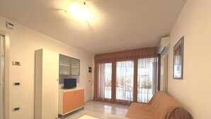 A living room with a sofa, a TV on a cabinet, and a large window with curtains. - Functional Apartment With a Spacious Fenced Garden (Grado)