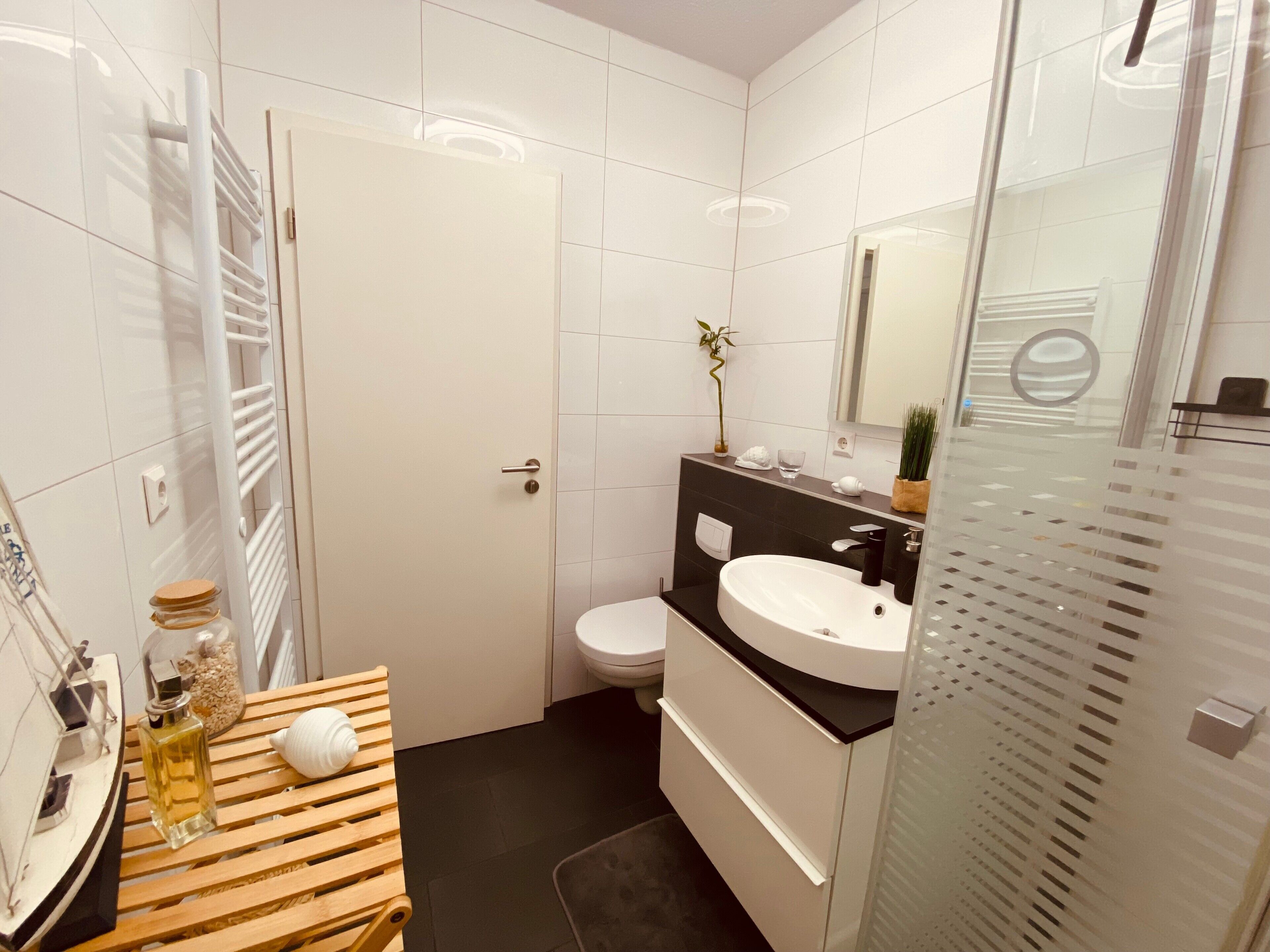 Casa de banho moderna com lavatório branco, bancada preta e cabine de duche em vidro.
