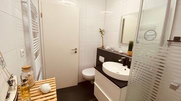 Casa de banho moderna com lavatório branco, bancada preta e cabine de duche em vidro.