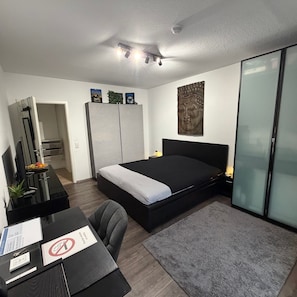 Une chambre moderne comprenant un lit, un bureau, une chaise, une armoire et une œuvre d’art accrochée au mur.