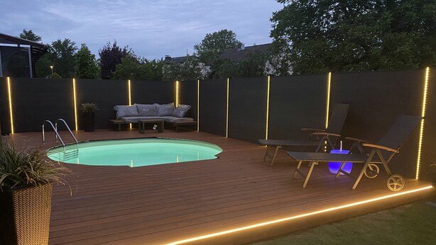 Un jardin avec une piscine, une terrasse en bois, des chaises longues et un canapé.
