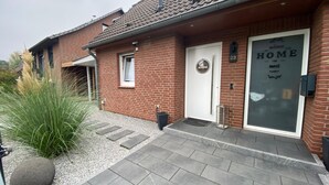 Une maison en briques avec un toit en tuiles, une porte d’entrée et une pancarte indiquant « Bienvenue ».