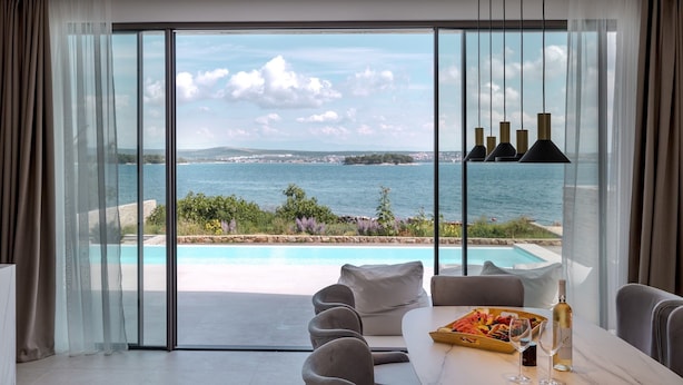 Habitación moderna con un gran ventanal corredera que da a una piscina y vistas al mar.