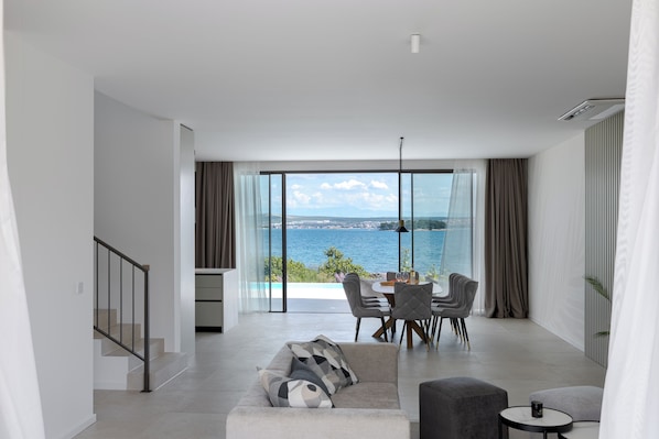 A modern living room with a view of the sea, a dining area, and a staircase.