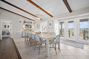 A spacious dining area with a large table and wicker chairs, a modern chandelier, and a view of the outdoors through large windows. - Oceanfront, Direct Beach Access, Panoramic Views - 510 Tarpon Blvd (Fripp Island)