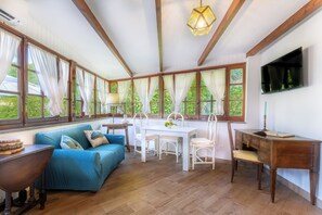 A room with a wooden ceiling, a dining table with chairs, a sofa, a desk, and a TV mounted on the wall. - Francesca's Guesthouse (Priora)