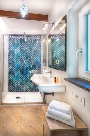 A bathroom with a glass shower enclosure, a white sink, a mirror, and a wooden vanity. - Francesca's Guesthouse (Priora)