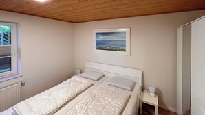 A bedroom with a single bed, a nightstand, a window, and a painting on the wall.