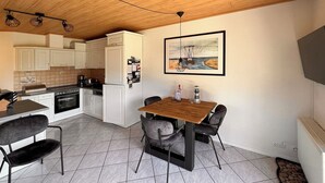 A compact kitchen with white cabinets, a wooden dining table with four chairs, and a tiled floor.