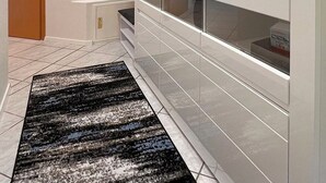 A hallway with a white cabinet, a black and white patterned rug, and a wooden door.