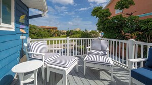 Una terrazza con sedie a righe bianche e azzurre e un tavolino, affacciata su una zona residenziale con case e vegetazione.