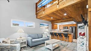 Un'ampia zona giorno con soffitto alto, una cucina dotata di elettrodomestici moderni e vista sulla spiaggia dalle finestre.