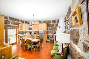 A cozy kitchen with stone walls, wooden cabinets, and a dining area with green upholstered chairs.