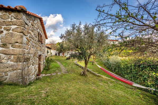 A stone building with a red-tiled roof, a grassy pathway, and a hammock.
