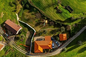 An aerial view of a property with a large orange-roofed building, a smaller adjacent structure, and a paved driveway with parked cars.