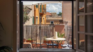 A view from a window to an outdoor patio with a round table and chairs, a bamboo fence, and buildings in the background. - Casa Mia - Trastevere Rooftop Loft (Roma)