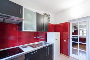 A modern kitchen with red tiles, a white refrigerator, and black cabinets. - Casa Mia - Trastevere Rooftop Loft (Roma)