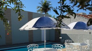 A poolside area with white metal chairs and umbrellas, a clear blue pool, and a stone wall in the background. - Hotéis Tropical Aquidauana (Aquidauana)
