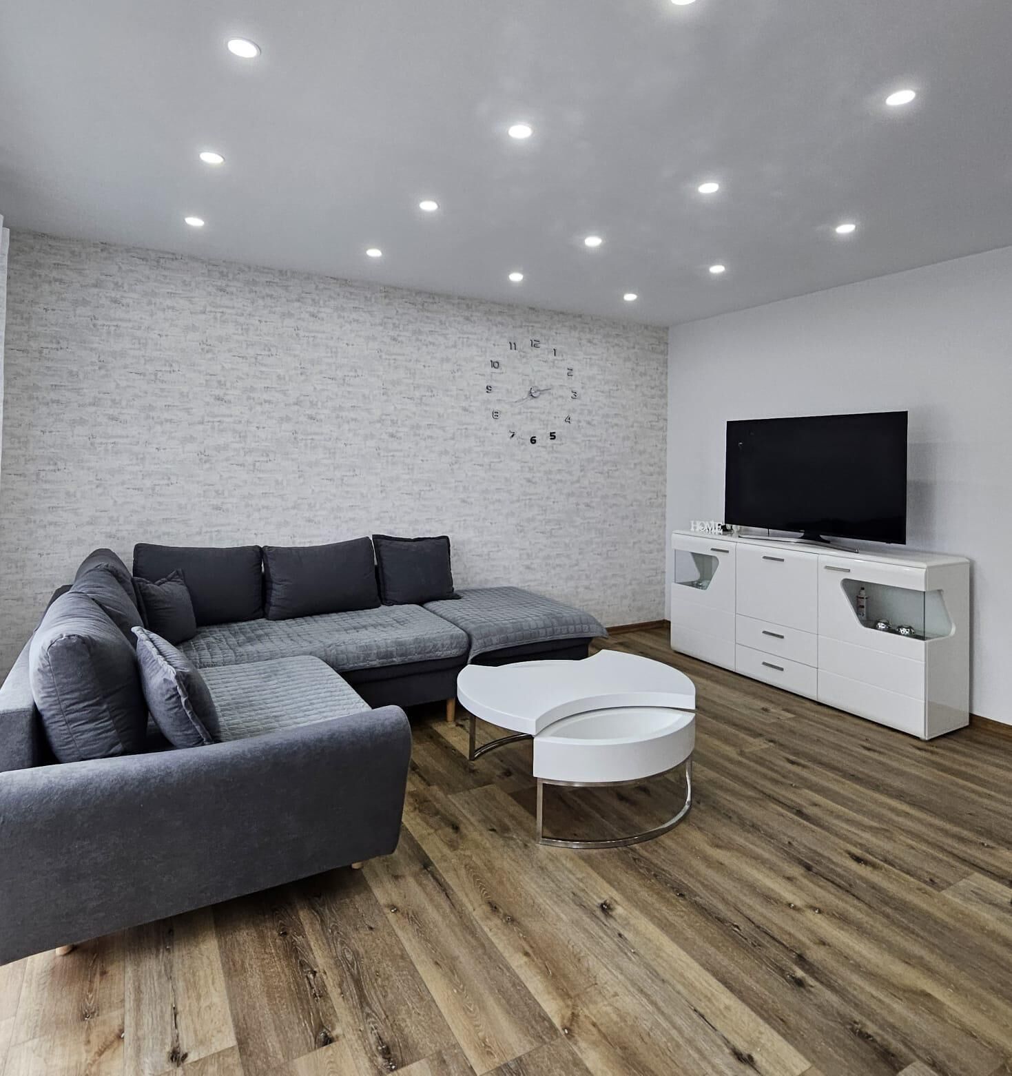 A modern living room with a sectional sofa, a white coffee table, and a TV on a white cabinet.