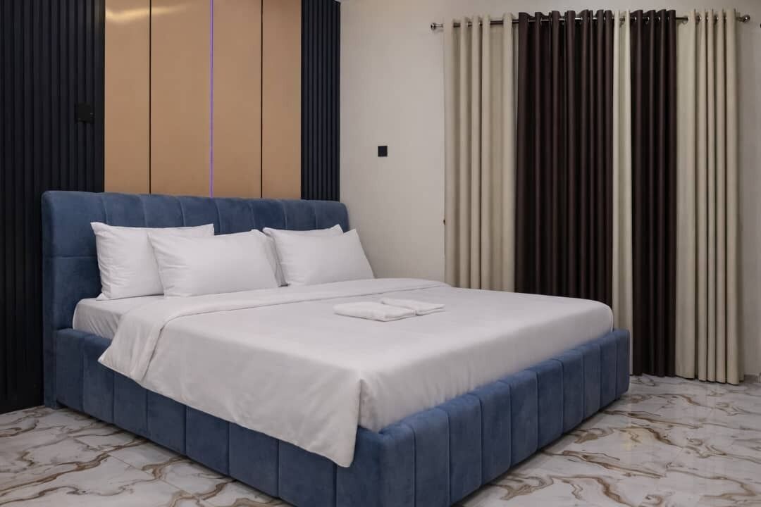 Un letto con una testiera blu, biancheria da letto bianca e un pavimento effetto marmo.