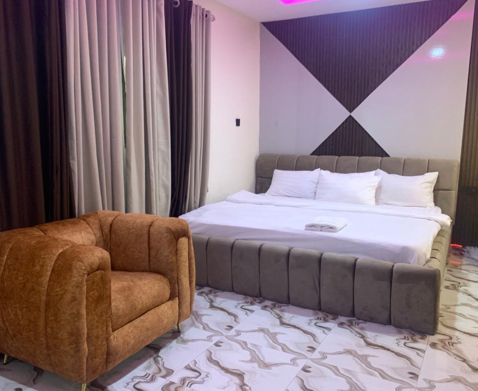 Un dormitorio con una cama, un sillón marrón y una alfombra estampada.