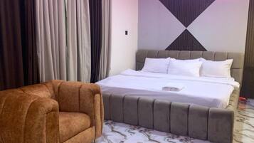 Un dormitorio con una cama, un sillón marrón y una alfombra estampada.