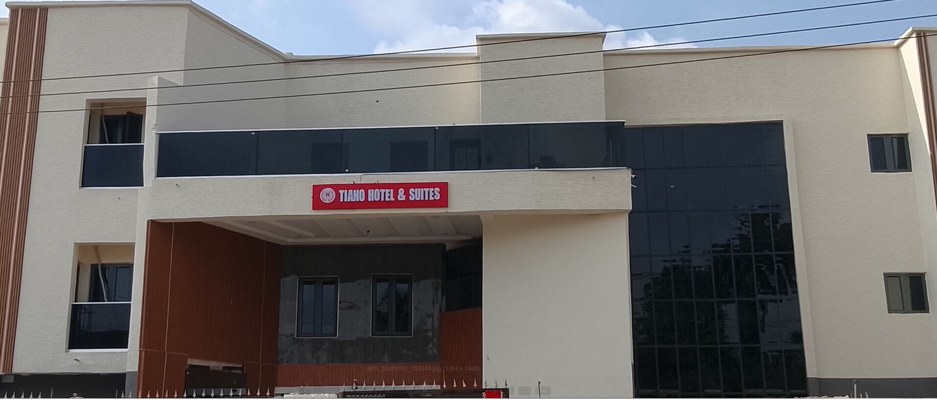 A hotel named "Tiano Hotel & Suites" with a modern facade, large windows, and a visible entrance.