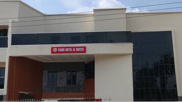 A hotel named "Tiano Hotel & Suites" with a modern facade, large windows, and a visible entrance.
