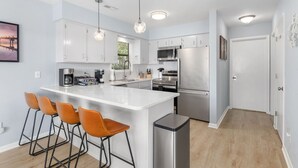 A modern kitchen with white cabinets, stainless steel appliances, and a central island with bar stools. - Ripple| Golf Cart · Private Beach · Outdoor Living (Emerald Isle)