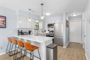 Une cuisine moderne avec des meubles blancs, des appareils en acier inoxydable et un îlot central doté de tabourets de bar.