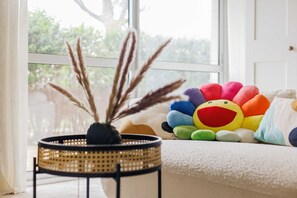 A cozy room with a large window, a wicker side table with a vase, and a colorful plush toy on a white sofa. - A Haven of Peace in Neuilly sur Seine (Neuilly-sur-Seine)
