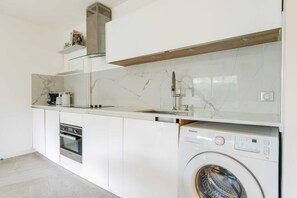 A modern kitchen with white cabinetry, a marble backsplash, a built-in oven, and a Samsung washing machine. - A Haven of Peace in Neuilly sur Seine (Neuilly-sur-Seine)