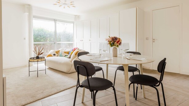 Un comedor moderno con una mesa redonda, sillas negras y un jarrón con flores.