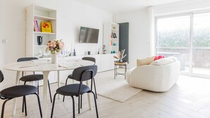 Una sala de estar moderna con un sofá blanco, una mesa de comedor con sillas y un televisor montado en la pared.
